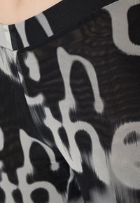 Mustat ja valkoiset kuviolliset legginsit, joissa on verkkotekstuuri, rohkea, abstrakti teksti ja kontrastivärinen musta vyötärö.
