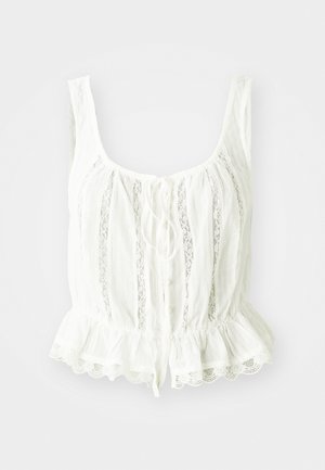 Blusa bianca con orlo a peplum, caratterizzata da bordi in pizzo, chiusura con cravatta e pieghe verticali. Realizzata in tessuto leggero, leggermente stropicciato.