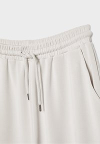 Lys grå træningsbukser med elastisk talje, snor med metalender og sidelommer. Blød, glat tekstur og enkelt design.