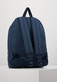 Zaino blu navy con spallacci imbottiti, tessuto testurizzato e fibbie laterali regolabili. Presenta una maniglia superiore per il trasporto.
