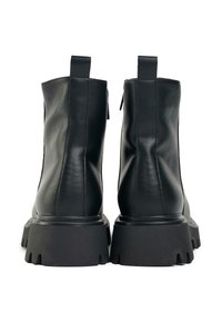 Black leather ankle boots with a structured design, rear zipper, and thick rubber soles featuring a jagged edge pattern.
