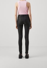 Jean skinny noirs taille haute, avec une texture lisse et des poches au dos, associés à un débardeur côtelé rose clair et des chaussures noires à clous.