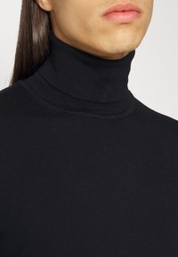 Czarny sweter z golfem wykonany z prążkowanej dzianiny. Ma wysoki kołnierz, dopasowany krój oraz gładką, równą teksturę.