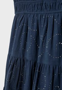 Tissu bleu foncé avec des volants froncés et de petits points argentés disposés en motifs étoilés subtils sur l'ensemble du matériau.