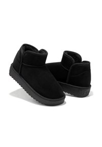 Botines negros de ante suave, con un caña corta, punta redondeada y suela de goma texturizada con un detalle del logo en el talón.