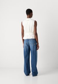 White sleeveless top with a cinched waist, paired with high-waisted, wide-leg blue denim jeans. Simple design with no visible patterns.