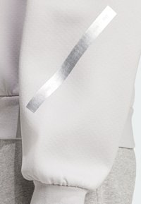 Sweat léger gris clair avec un poignet côtelé, comportant une bande réfléchissante argentée sur la manche indiquant les années 2015 à 2021.