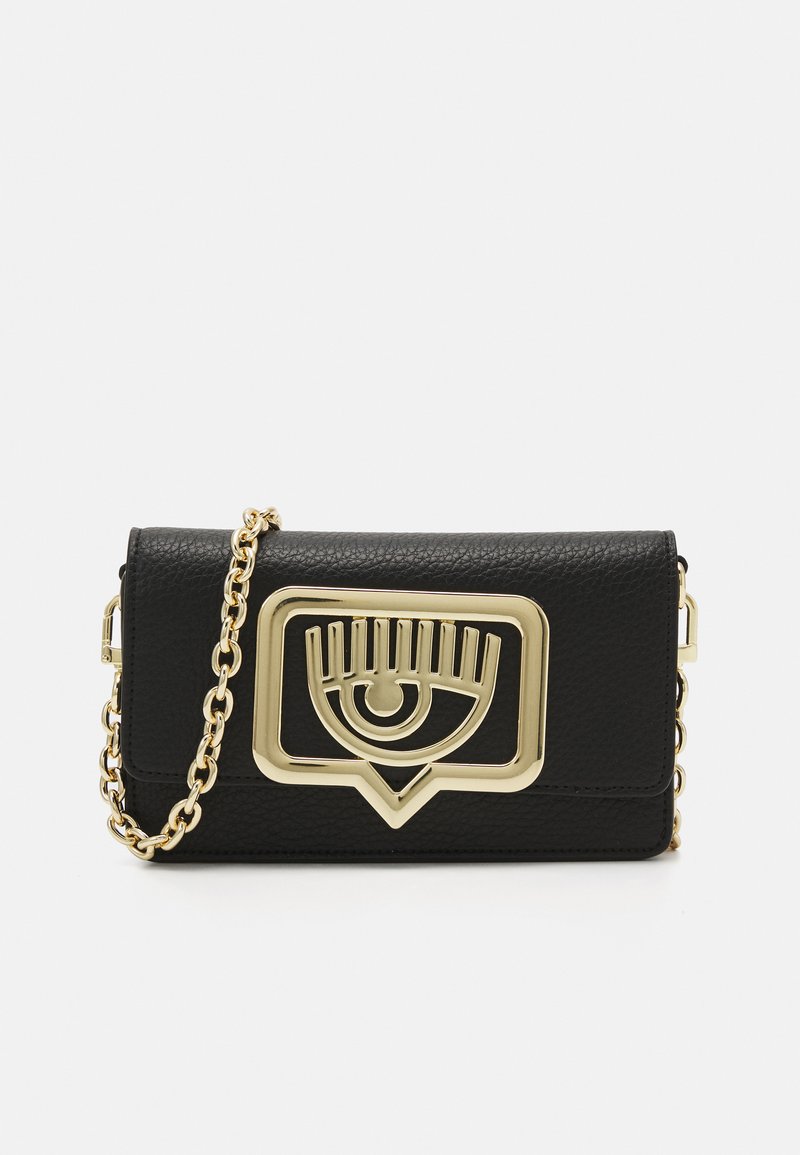 Borsa a mano in pelle nera con un accento metallico dorato a forma di occhio, dotata di una tracolla a catena e di una forma rettangolare. Superficie texturizzata con una finitura lucida.