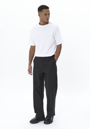 White short-sleeve t-shirt paired with black loose-fitting trousers and black shoes, set against a plain white background.