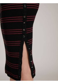 Robe en maille côtelée noire avec des rayures horizontales rouges, dotée d'une fente latérale avec des boutons argentés et des œillets le long de l'ouverture.