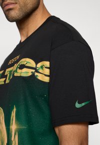 Μαύρο βαμβακερό T-shirt με πράσινο και χρυσό γραφικό των "Boston Celtics" και πράσινο λογότυπο της Nike στο αριστερό μανίκι.