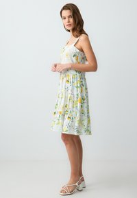 Bloemenjurk met een citroenenpatroon, witte achtergrond, gelaagd ontwerp en dunne bandjes; aangevuld met lichtgekleurde block-heeled sandalen.