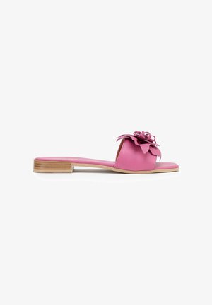 Sandalia plana rosa con tacón bajo de madera y flor decorativa en capas en la amplia tira frontal sobre fondo blanco.