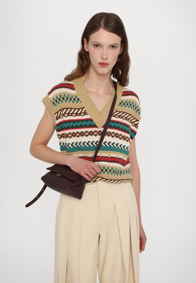 Suéter de punto en beige con patrones geométricos multicolores, escote en V y mangas cortas. Combinado con pantalones ligeros con pliegues y un bolso cruzado oscuro.