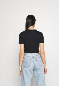 Svart kortärmad t-shirt med rund halsringning, kombinerad med ljusblå denimjeans med bakfickor och en läderpatch på midjan.