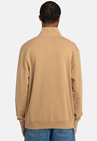 Felpa beige con colletto alto, polsini e orlo a costine, e una consistenza morbida. Il retro è semplice, con una vestibilità rilassata.