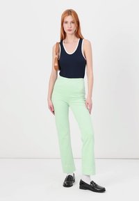 Ναυτικό αμάνικο μπλουζάκι με λευκή ραφή, συνδυασμένο με ανοιχτό πράσινο παντελόνι σε ευθεία γραμμή. Το μοντέλο φορά μαύρες loafer και κρατά καφέ τσάντα ώμου.