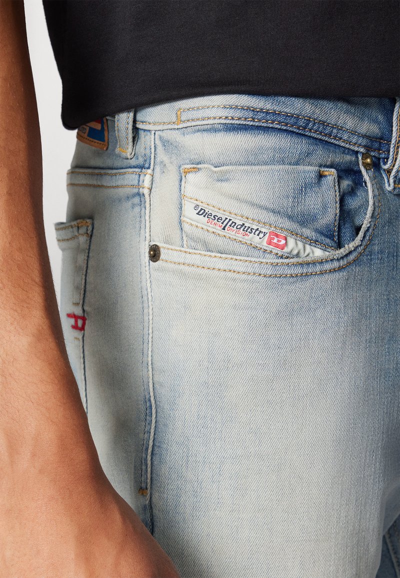 Lichtblauwe jeans met een vervaagde was, met een voorzak en rode stikseldetails, een zichtbaar merklabel aan de zijkant, gemaakt van denim materiaal.