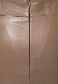 Jupe en cuir beige avec une texture lisse, présentant une couture verticale et une fermeture éclair en haut. Design minimaliste.