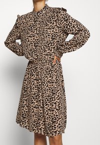 Vestido de estampado de leopardo en tonos marrones y negros, con una cintura ajustada, mangas largas con puños fruncidos y un cuello alto.
