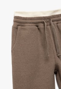 Braune Jogginghosen aus Waffelstrick mit einem cremefarbenen elastischen Bund, der eine Kordelzug und Seitentaschen bietet. Der strukturierte Stoff verleiht Dimension.