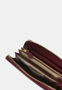 Portafoglio in pelle bordeaux con cerniera dorata, dotato di più scomparti e una texture liscia. L'interno ha una fodera beige e slot per schede.