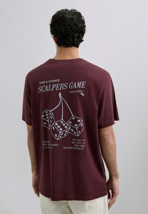 Camiseta burdeos de manga corta con un gráfico de dados y texto. La parte posterior incluye los detalles del evento en imprenta blanca. Material de algodón.