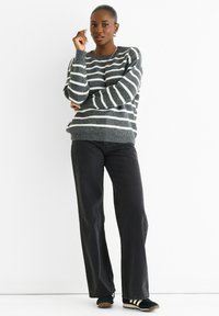 Knitted gray sweater with white stripes, crew neck, loose fit. Paired with black wide-leg jeans and black sneakers with white accents.