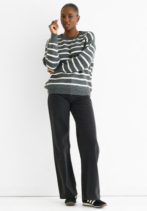 Knitted gray sweater with white stripes, crew neck, loose fit. Paired with black wide-leg jeans and black sneakers with white accents.