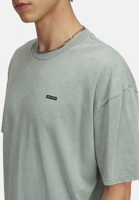 Lys grøn bomulds T-shirt med en afslappet pasform, rund halsudskæring, op-snoede ærmer og et lille sort "Under Armour" logo på fronten.