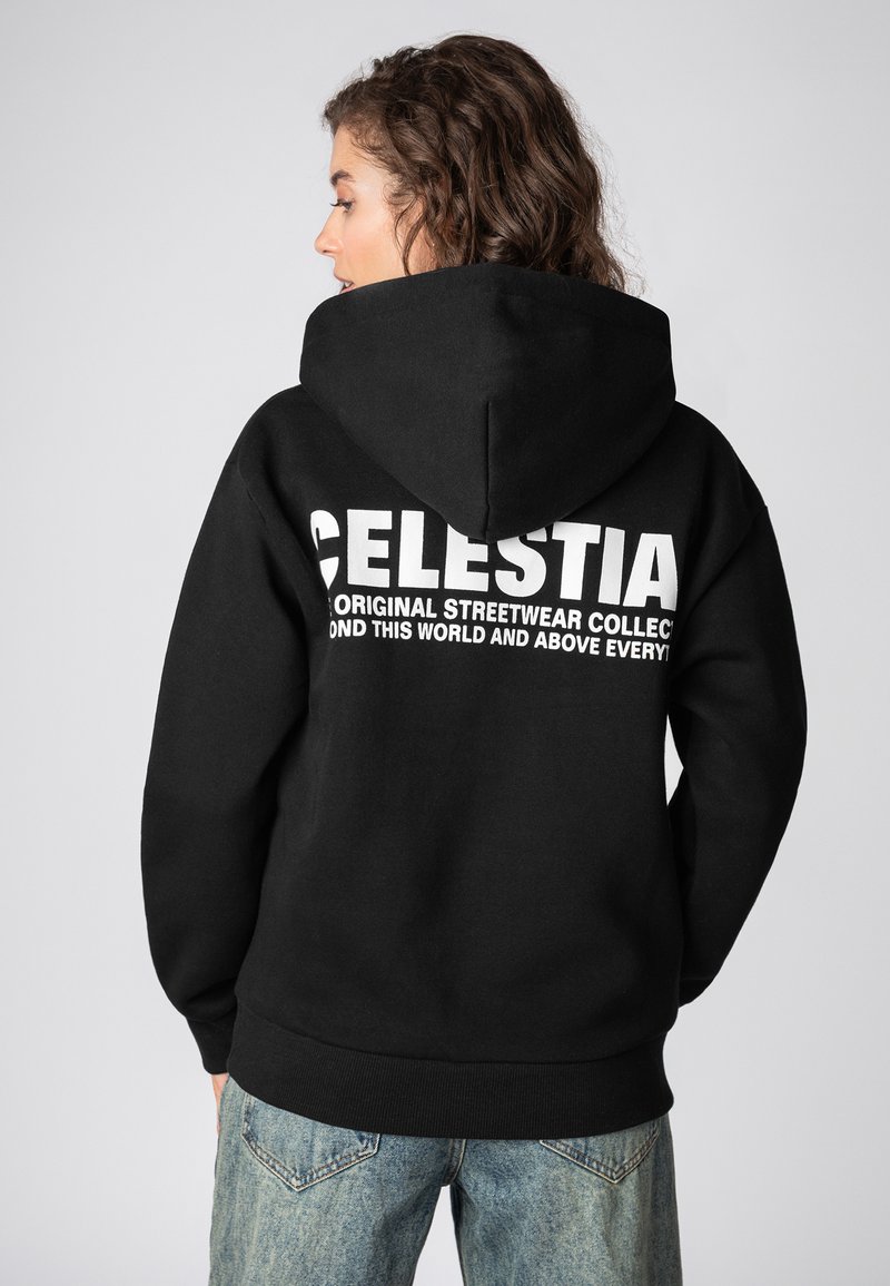 Schwarzer Kapuzenpullover mit großem weißem Text auf dem Rücken, verfügt über einen lockeren Schnitt und gerippte Bündchen. Trägt man mit hellblauen Jeans.