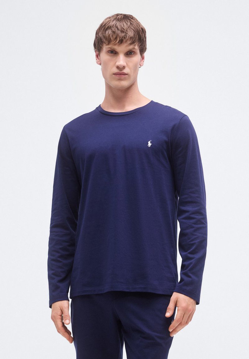 Camisa de manga comprida azul-marinho feita de algodão macio. Apresenta gola redonda e um pequeno logótipo branco no peito. Textura suave.