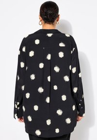 Sort bluse med store cremefarvede polkaprikker, knappede manchetter og en plissering bagpå for ekstra stil. Blød stofstruktur, lange ærmer.