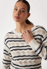 Cremfarbener, feingestrickter Pullover mit navyblauen horizontalen Streifen und einem wellenförmigen Muster. Rippstrickbündchen und der Halsausschnitt verleihen dem Design eine interessante Textur.