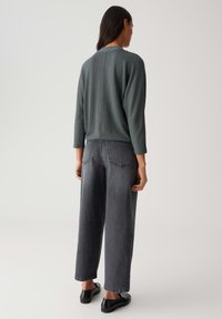 Maglione verde a coste con scollo rotondo, abbinato a jeans in denim grigi larghi e scarpe nere flat.