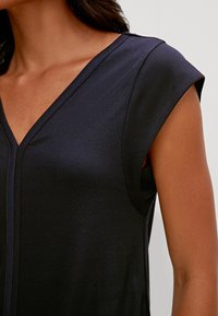 Top senza maniche blu navy con scollo a V. Realizzato in tessuto liscio, presenta dettagli di cuciture sottili lungo il collo e le aperture delle braccia.