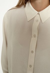 Heledbeez, pikka varrukaga särk, mis on valmistatud tekstuuriga kangast. Omab teravat kraed ja kuut nuppu ees.