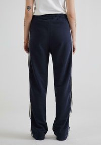 Mørkeblå sweatpants med en afslappet pasform, der har hvide sideløsninger, elastisk talje og en glat, blød tekstur.