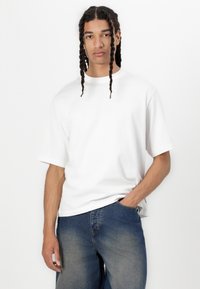 Hvit bomull T-skjorte med korte ermer, rund hals og avslappet passform, sammen med mørkeblå jeans; glatt tekstur og enkelt design.