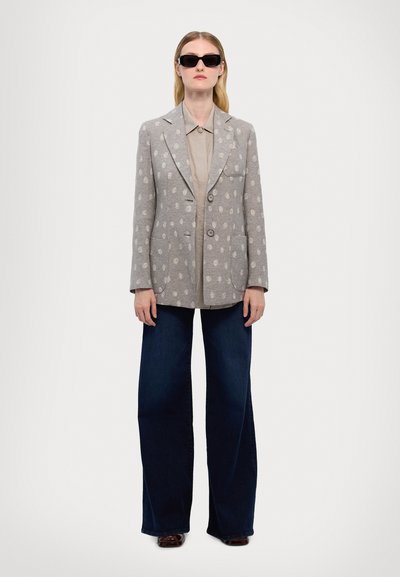 Gray patterned blazer with large lapels, double buttons, and two front pockets, paired with a light collared shirt and dark flared jeans.