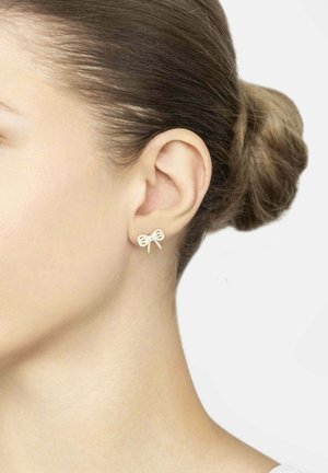 Gold-tone stud earrings shaped like a bow, featuring a textured finish and small loop accents, displayed on a model's ear.