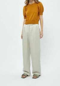 Senapsgul kortärmad topp med ribbad struktur, kombinerad med krämfärgade vida byxor med framfåll. Bärs med olivgröna sandaler.