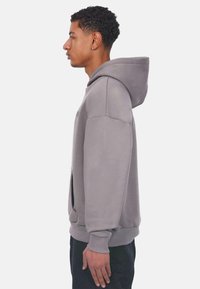 Grey hooded sweatshirt with a relaxed fit, featuring a front pocket and ribbed cuffs. Smooth texture, minimalistic design.