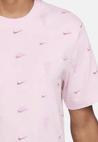 T-shirt rose à manches courtes en coton, avec un motif de logo répété en rose foncé. Encolure ronde, texture douce, design décontracté.