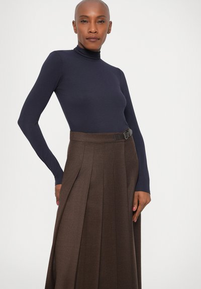 Marineblå turtleneck-top båret med en højtaljet, brun plisseret nederdel med et sort bælte. Glat stoftekstur, struktureret design.