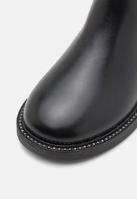 Czarne skórzane botki za kostkę o gładkiej fakturze, okrągłym nosku, dekoracyjnym koralikowym wykończeniu wzdłuż podeszwy oraz matowym, kontrastowym wykończeniu.