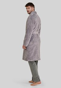 Bata de baño gris en espiga con cuello y cinturón, combinada con pantalones grises suaves. La tela tiene una textura aterciopelada, que mejora la comodidad.