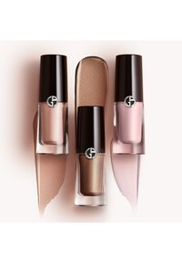 Trois flacons de vernis à ongles avec des bouchons noirs et un logo, présentant des teintes de rose clair, de nude et de bronze, accompagnés de nuances assorties.