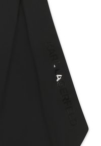 Un tissu noir à texture lisse présente un logo "KARL LAGERFELD" brillant le long du bord, soulignant un design épuré et contemporain.