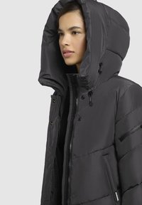 Must must, mille suure kapuutsiga, lukuga, nupuga ja küljetaskutega. Omab tikitud tekstuuri ja reguleeritavaid nööre.